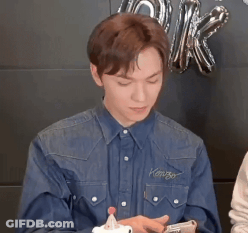 A Young Man In A Denim Shirt Is Holding A Cell Phone . GIF