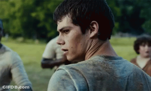 A Young Man In A Dirty Shirt Is Standing In A Field Looking At The Camera . GIF