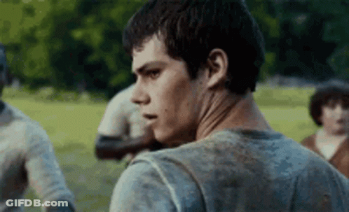 A Young Man In A Dirty Shirt Is Standing In A Field With Other People . GIF