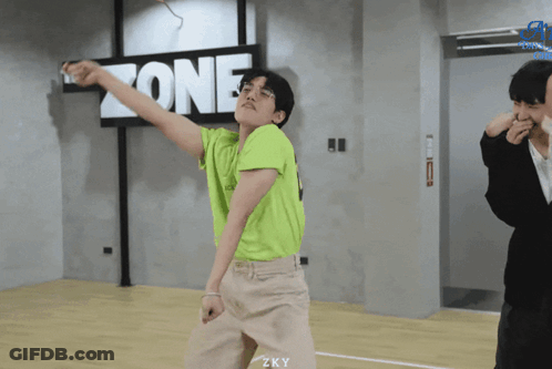 A Young Man In A Green Shirt Is Dancing In Front Of A Sign That Says Zone GIF