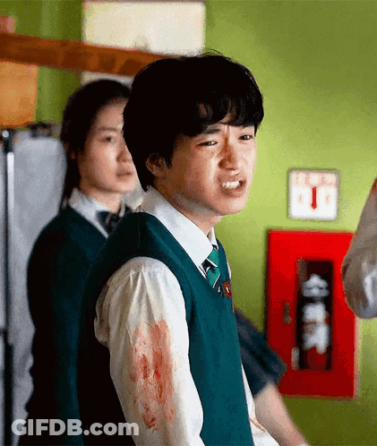 A Young Man In A Green Vest And Tie Is Standing In A Room With Blood On His Shirt . GIF