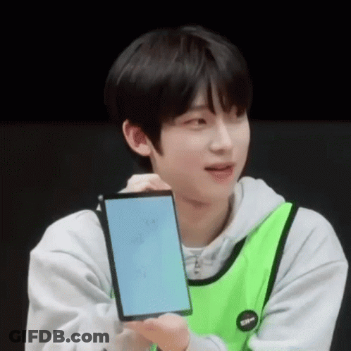 A Young Man In A Green Vest Is Holding A Cell Phone . GIF