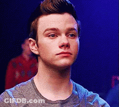 A Young Man In A Grey Shirt Is Looking At The Camera With A Serious Look On His Face . GIF