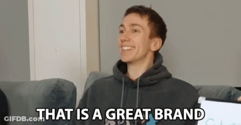 A Young Man In A Hoodie Is Sitting On A Couch And Smiling . GIF