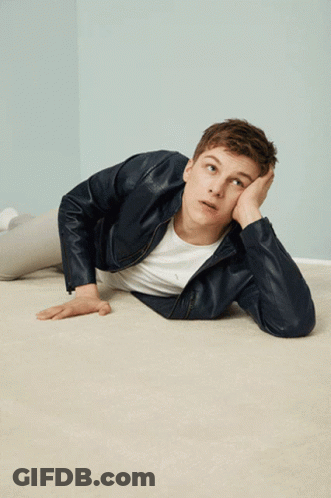 A Young Man In A Leather Jacket Is Laying On The Floor With His Hand On His Face GIF