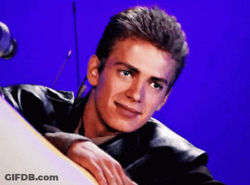 A Young Man In A Leather Jacket Is Leaning On A Table And Smiling . GIF