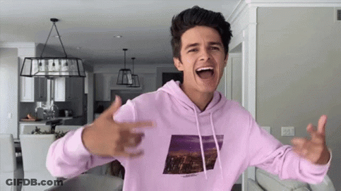A Young Man In A Pink Hoodie Is Standing In A Living Room With His Arms Outstretched . GIF