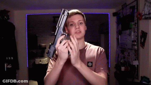 A Young Man In A Pink Shirt Holds A Gun In His Hands GIF