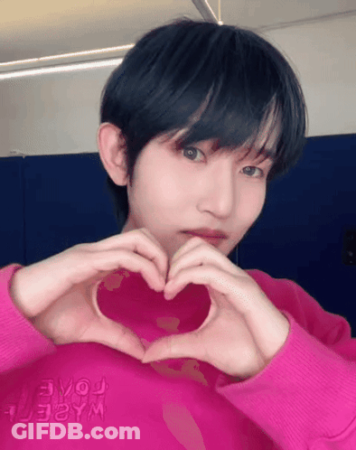 A Young Man In A Pink Shirt Is Making A Heart Shape With His Hands GIF