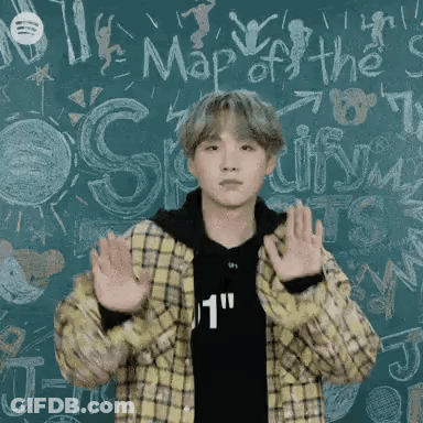 A Young Man In A Plaid Jacket Is Standing In Front Of A Blackboard With His Hands In The Air . GIF