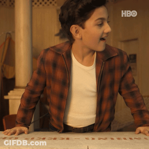 A Young Man In A Plaid Jacket Is Standing Next To A Box That Says Hbo On It GIF