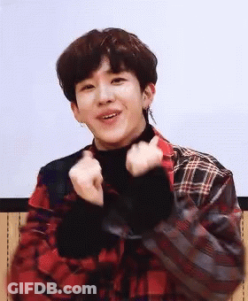 A Young Man In A Plaid Shirt Is Making A Heart Shape With His Hands And Smiling . GIF