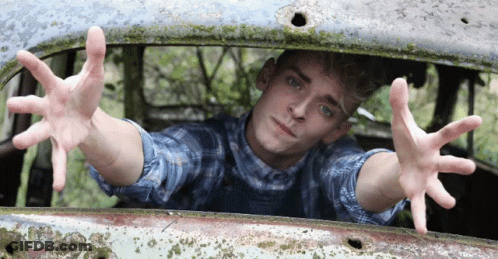 A Young Man In A Plaid Shirt Is Reaching Out From A Rusted Car Window GIF