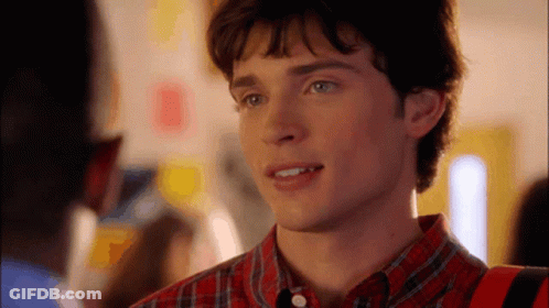 A Young Man In A Plaid Shirt Is Smiling And Looking At Something GIF
