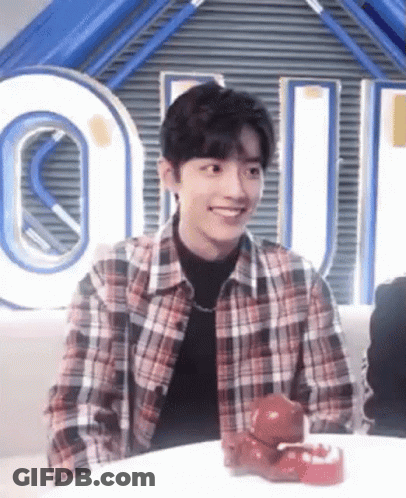 A Young Man In A Plaid Shirt Is Smiling While Sitting At A Table With A Toy On It . GIF