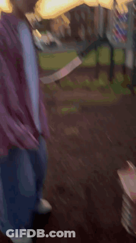 A Young Man In A Plaid Shirt Is Standing In Front Of A Slide In A Park GIF
