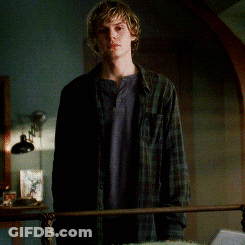 A Young Man In A Plaid Shirt Is Standing Next To A Bed GIF