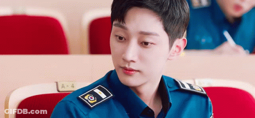 A Young Man In A Police Uniform Is Sitting In A Lecture Hall And Looking At The Camera . GIF