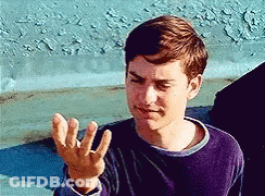 A Young Man In A Purple Shirt Is Making A Funny Face With His Hand . GIF