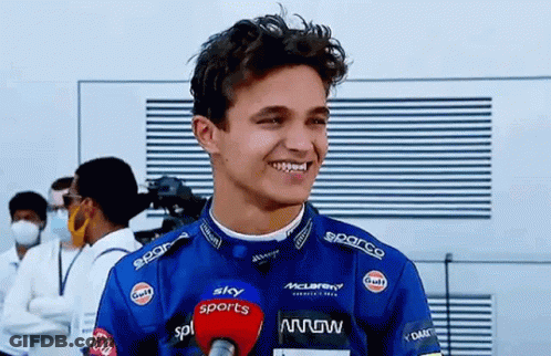 A Young Man In A Racing Suit Is Talking Into A Microphone And Smiling . GIF