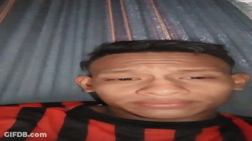 A Young Man In A Red And Black Striped Shirt Is Making A Face GIF