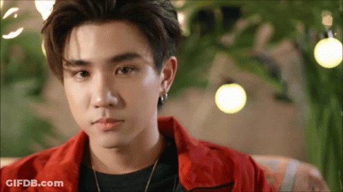 A Young Man In A Red Jacket Is Sitting On A Couch Looking At The Camera . GIF