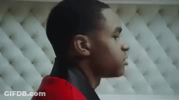 A Young Man In A Red Jacket Is Standing In Front Of A White Couch . GIF