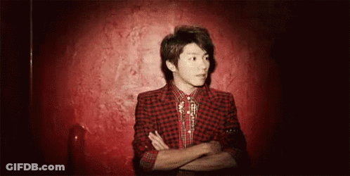 A Young Man In A Red Plaid Jacket And Tie Is Standing In Front Of A Red Wall With His Arms Crossed . GIF