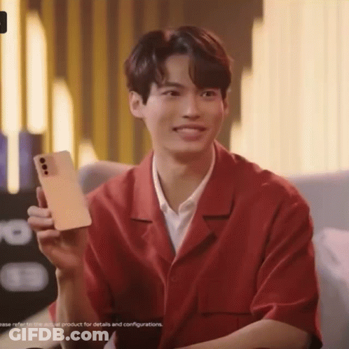 A Young Man In A Red Shirt Is Holding A Cell Phone In His Hand . GIF