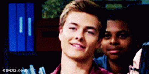 A Young Man In A Red Shirt Is Smiling While Standing Next To Another Man . GIF