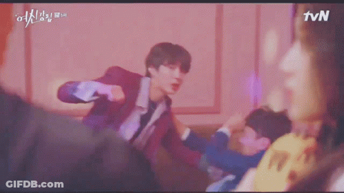 A Young Man In A Red Suit Is Standing In Front Of A Pink Wall And Looking At The Camera . GIF