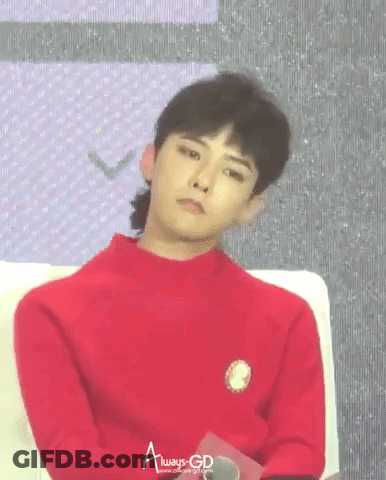 A Young Man In A Red Sweater Is Sitting On A Couch And Looking At The Camera . GIF