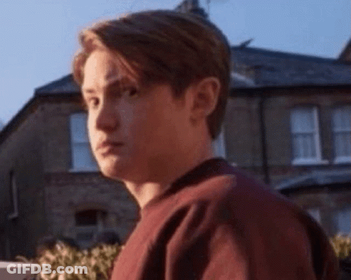 A Young Man In A Red Sweater Is Standing In Front Of A House . GIF