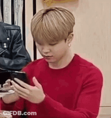 A Young Man In A Red Sweater Is Using A Cell Phone . GIF