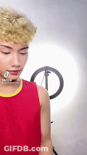 A Young Man In A Red Tank Top With A Yellow Stripe Has A Tik Tok Sticker On His Face GIF