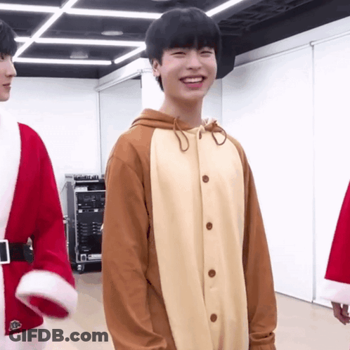 A Young Man In A Reindeer Costume Is Smiling In A Room GIF