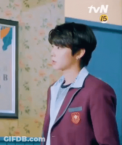 A Young Man In A School Uniform Is Standing In A Room With A Picture On The Wall . GIF