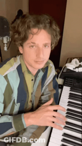 A Young Man In A Striped Shirt Is Playing A Piano In A Room . GIF