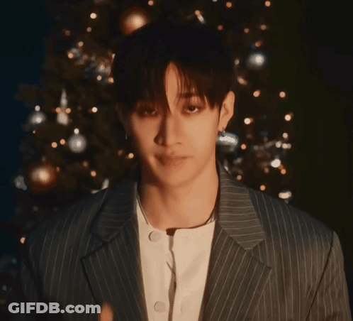 A Young Man In A Striped Suit Giving A Thumbs Up In Front Of A Christmas Tree GIF