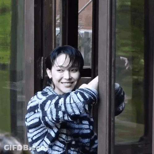 A Young Man In A Striped Sweater Is Smiling While Standing In A Doorway . GIF
