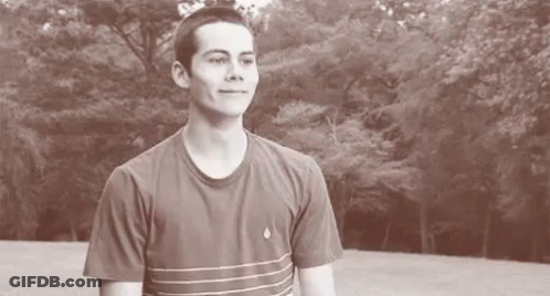 A Young Man In A Striped T-Shirt Is Standing In Front Of A Forest . GIF