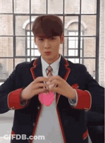 A Young Man In A Suit And Tie Is Holding A Pink Heart In His Hands . GIF