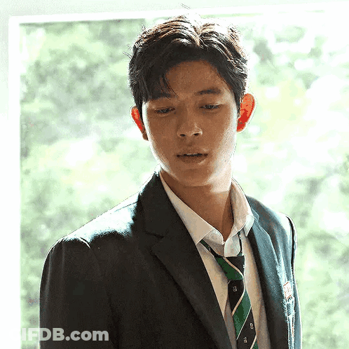 A Young Man In A Suit And Tie Is Looking Out Of A Window . GIF