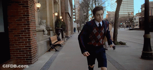 A Young Man In A Suit And Tie Is Running Down A Sidewalk In A City . GIF