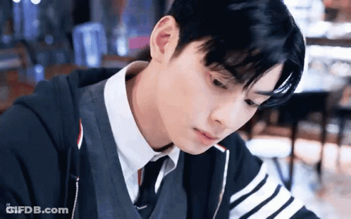 A Young Man In A Suit And Tie Is Sitting At A Table Looking Down . GIF
