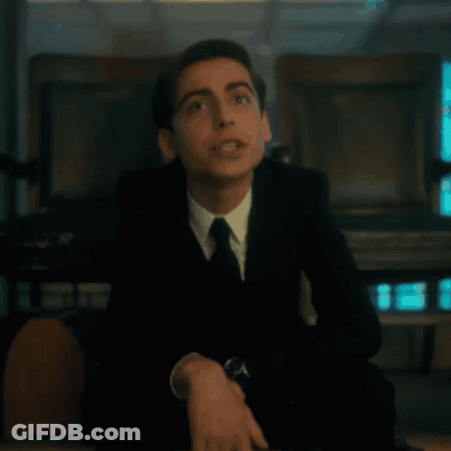 A Young Man In A Suit And Tie Is Sitting On A Chair . GIF