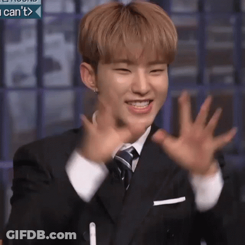 A Young Man In A Suit And Tie Is Smiling And Waving His Hands In The Air . GIF