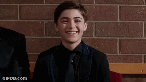 A Young Man In A Suit And Tie Is Smiling While Sitting On A Bench . GIF