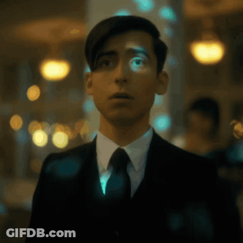A Young Man In A Suit And Tie Is Standing In A Dark Room . GIF