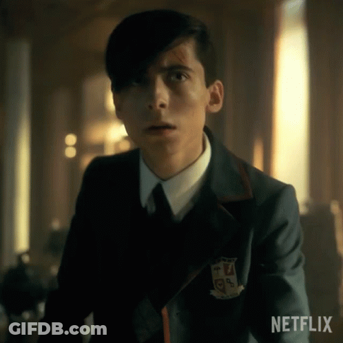 A Young Man In A Suit And Tie Is Standing In A Room Looking At The Camera . GIF